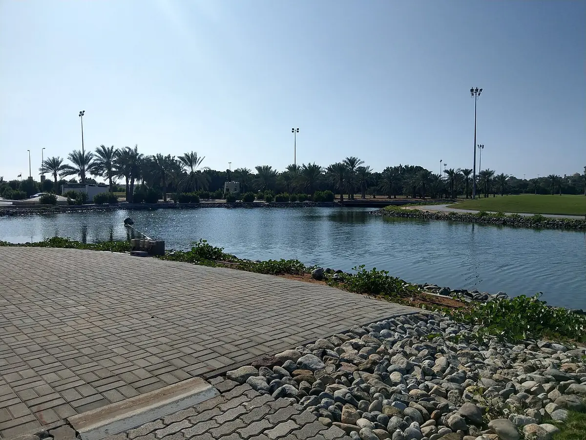 Un chemin pavé longeant un bassin bordé de palmiers dans un parc de Ras Al Khaimah