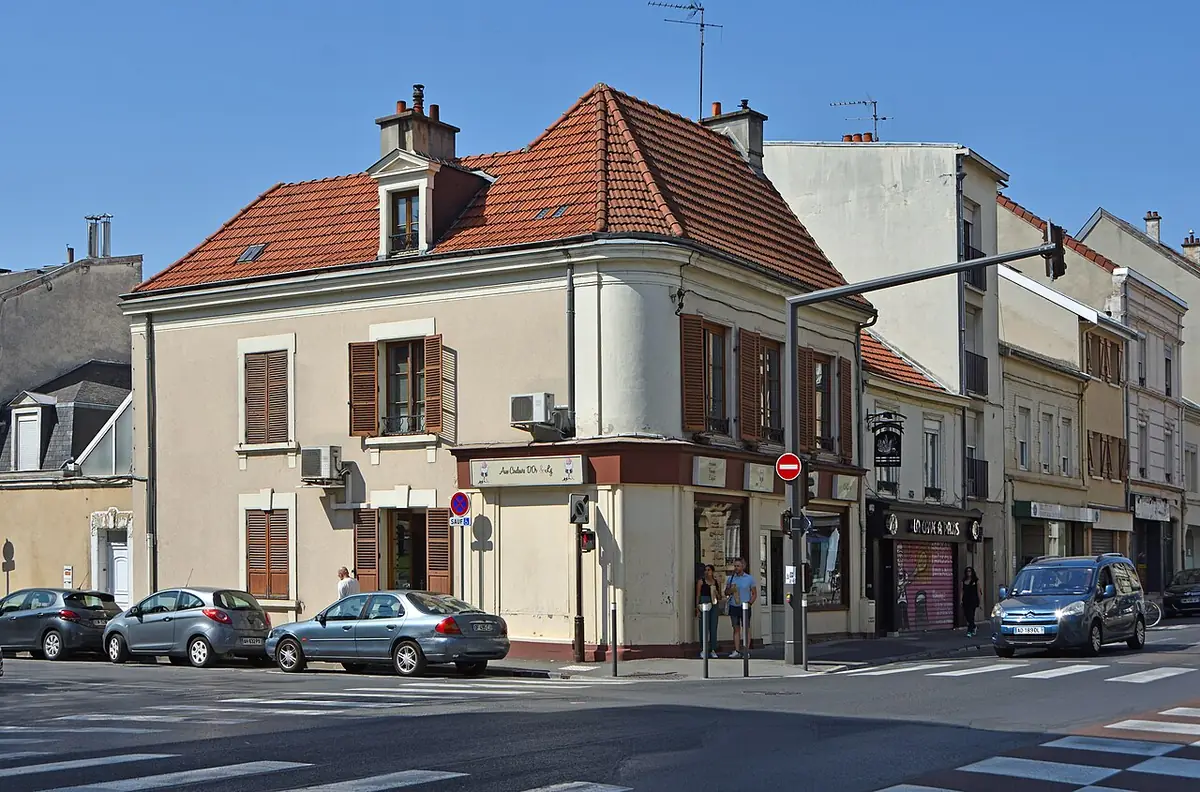 Un immeuble d’angle avec toit en tuiles rouges et commerces au rez-de-chaussée