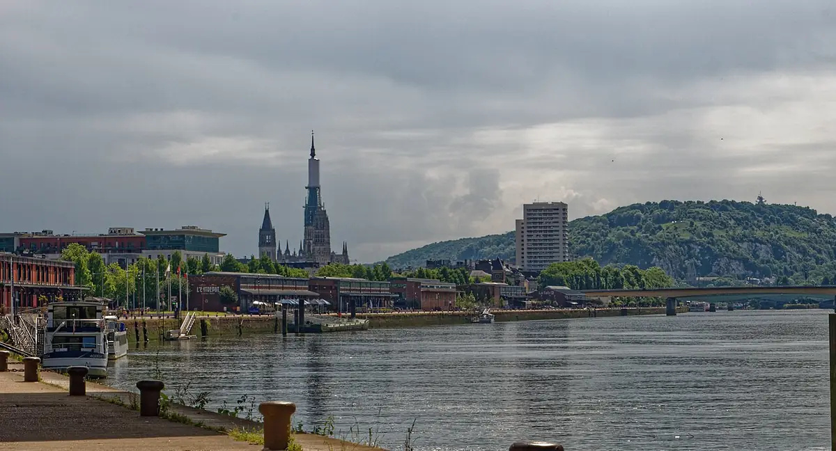 La Seine à Rouen sous un ciel gris, flèche de la cathédrale et collines boisées à l’horizon