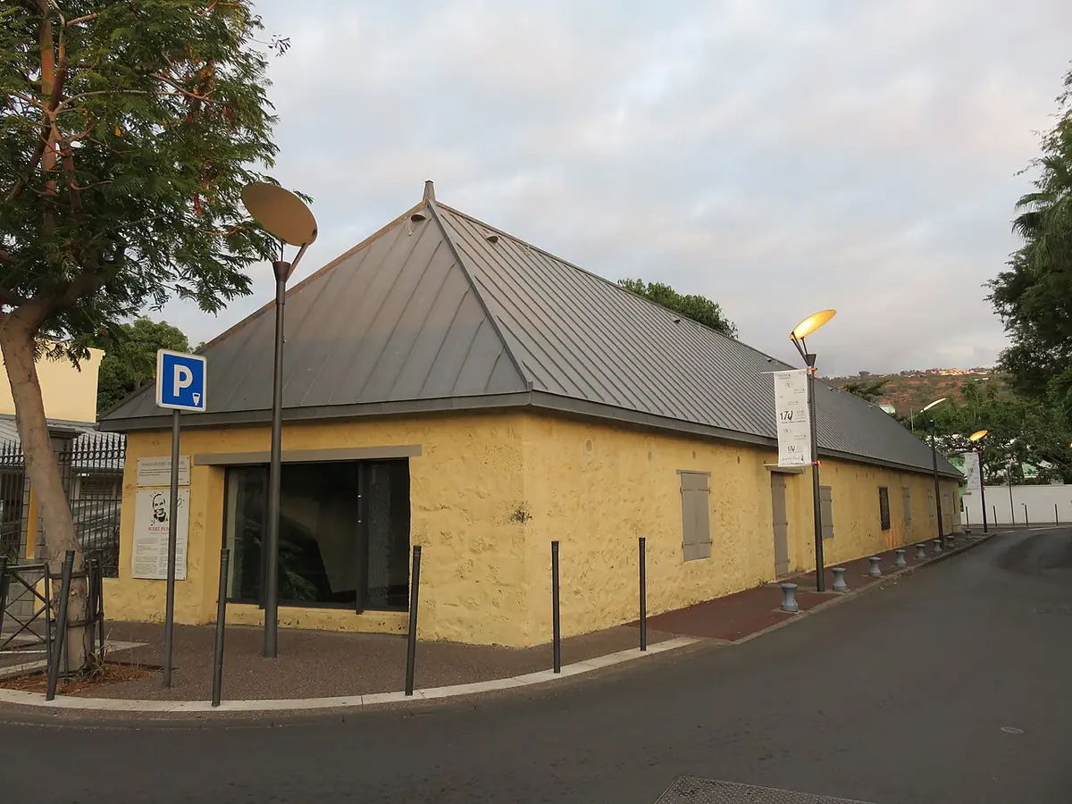 La longère communale de Saint-Paul aux murs jaunes et toit de tôle, au coin d’une rue