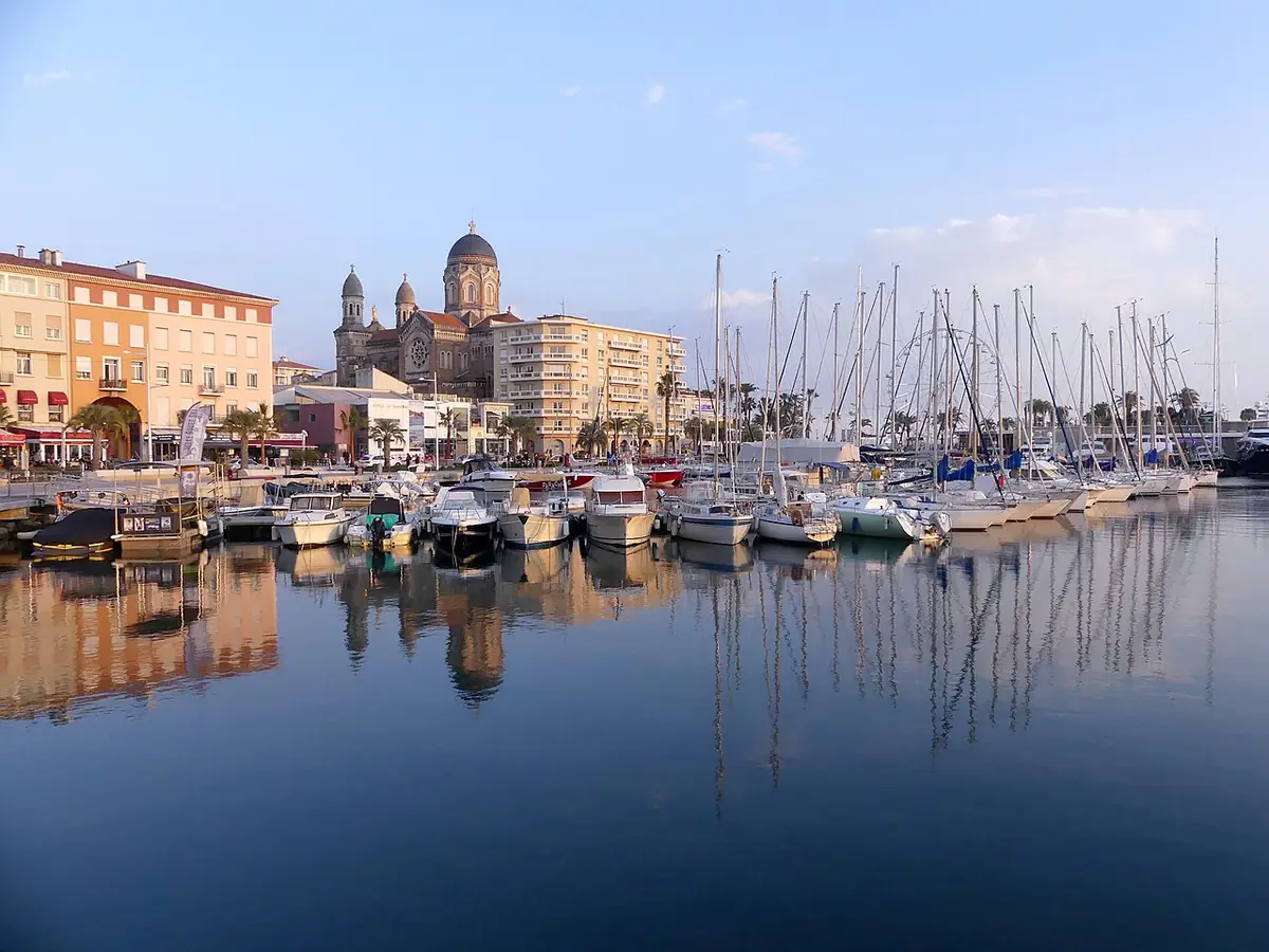Port de Saint-Raphaël en soirée, voiliers reflétés dans l’eau et basilique au fond