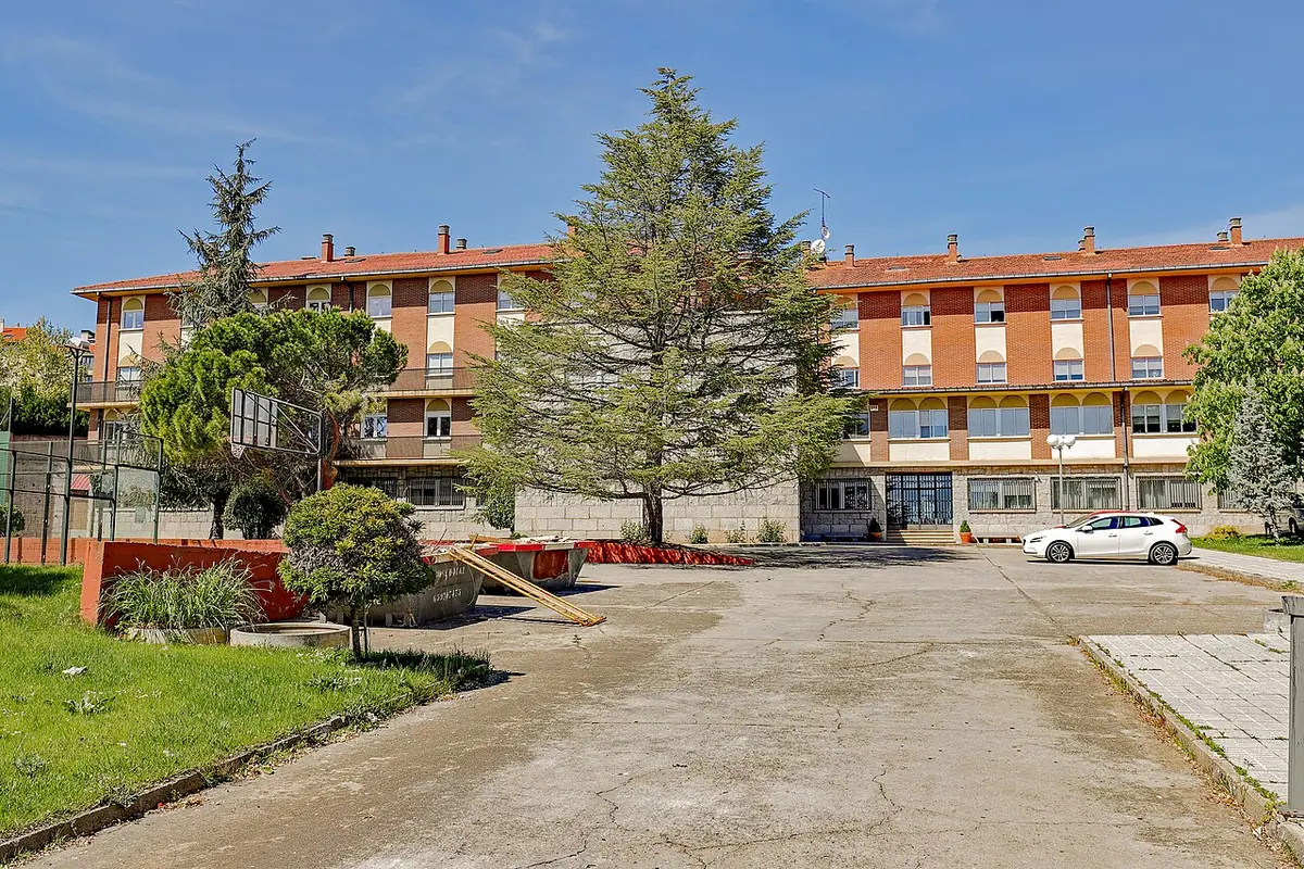 Bâtiment en brique à deux étages derrière des arbres et une cour à Salamanque