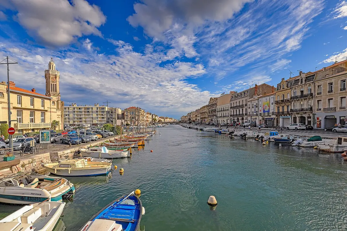 Un canal de Sète bordé de façades colorées et de bateaux amarrés, clocher d’église à gauche