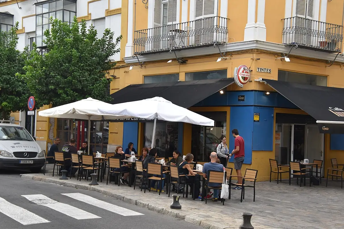 Terrasse de café sous des parasols au pied d’un immeuble jaune à balcons en fer forgé