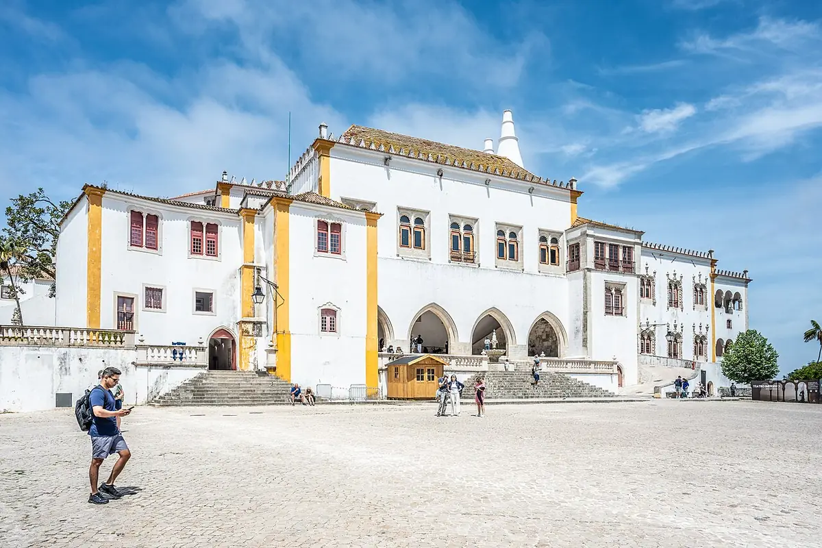 Le palais national de Sintra, façade blanche et jaune et sa cheminée conique, devant une place pavée