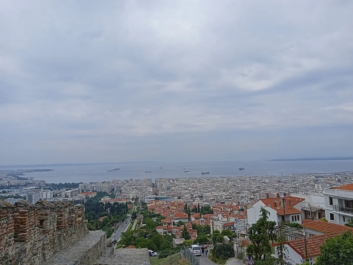 Vue en hauteur sur les toits de Thessalonique et la mer, des remparts au premier plan, sous un ciel nuageux