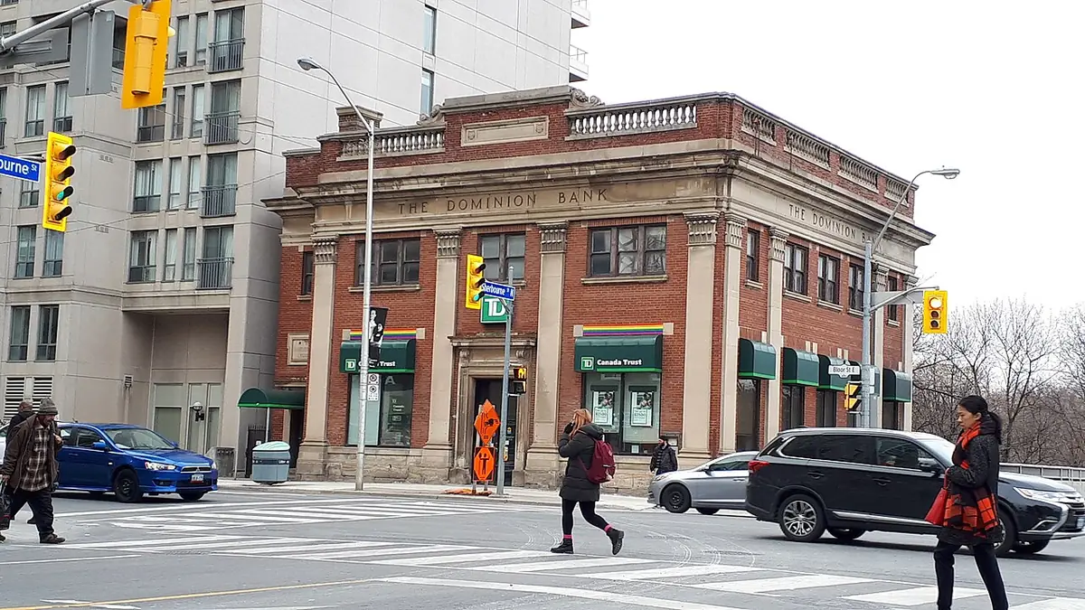 Un bâtiment bancaire patrimonial à l’angle d’une rue animée de Toronto, avec des piétons