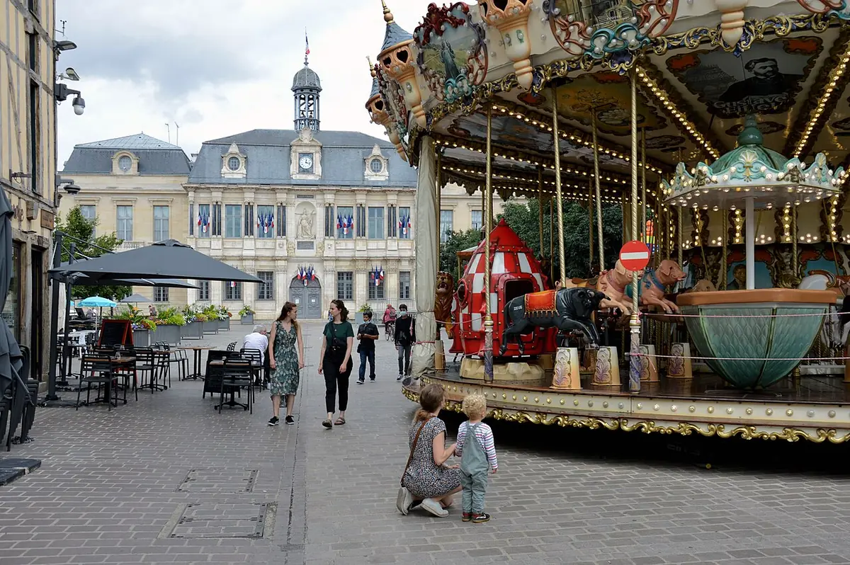 Un manège sur la place du Maréchal-Foch, un bâtiment à campanile en arrière-plan