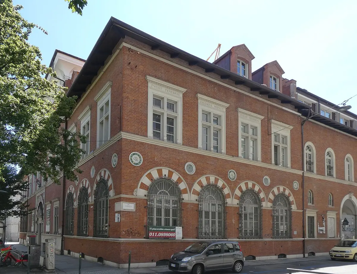 Un immeuble en briques rouges à arcades, à l’angle d’une rue du corso Raffaello à Turin