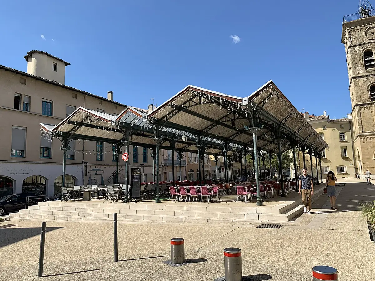 La halle métallique de la place Saint-Jean entourée d’immeubles, clocher de l’église à droite