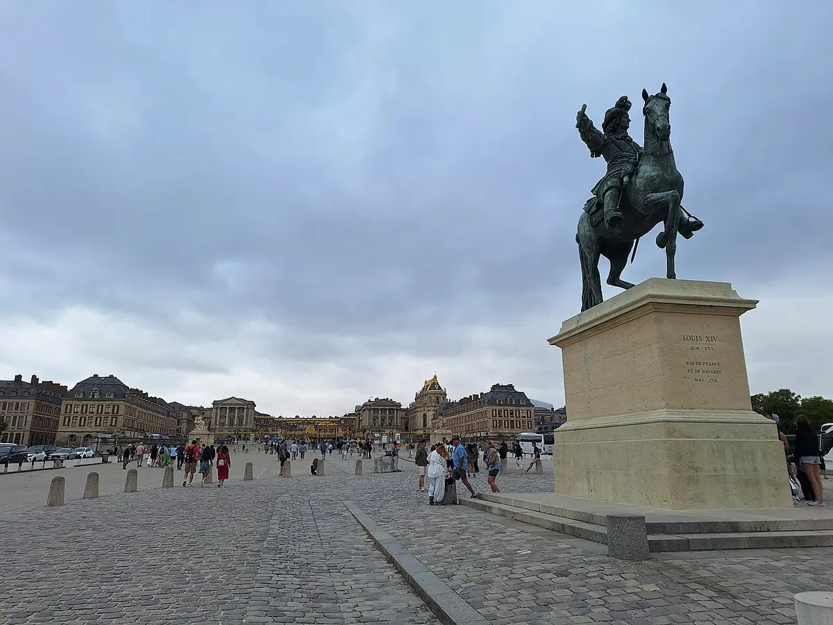 Une statue équestre sur l’esplanade pavée devant le château de Versailles