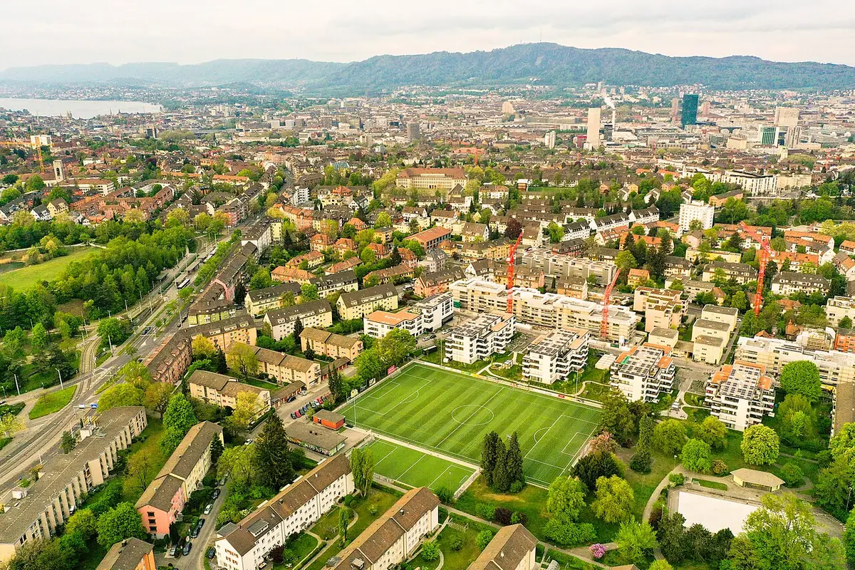 Vue aérienne de Zurich entre habitations, champs verts et montagnes au loin